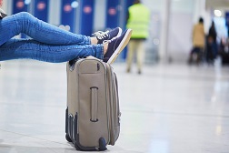 Frau sitzt am Flughafen, hat ihre Beine auf ihren Koffer gelegt