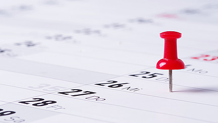 Eine rote Stecknadel steckt in einem Kalender.