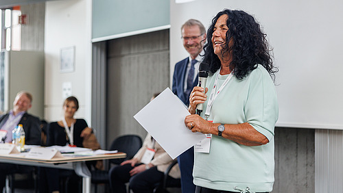 A woman holds a certificate and a microphone in her hands and thanks for an award. 