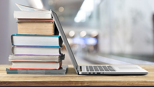 Ein aufgeklappter Laptop und ein Stapel B&uuml;cher