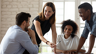 Eine Frau erkl&auml;rt Personen, die am Tische sitzen die Arbeitsergebnisse.