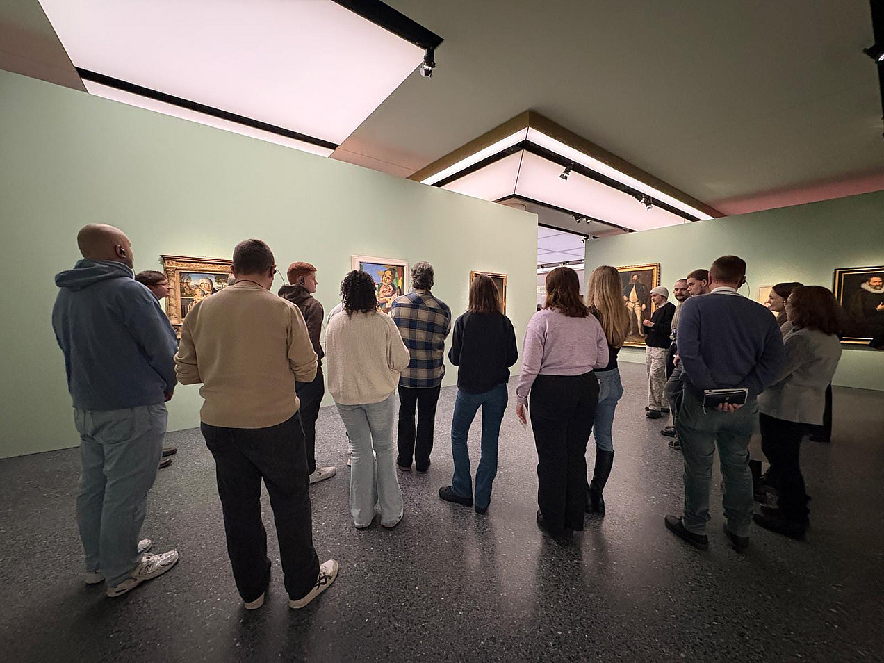 Das Bild zeigt eine Gruppe Menschen von hinten in einer Kunstausstellung vor einer hellgr&uuml;nen Wand.