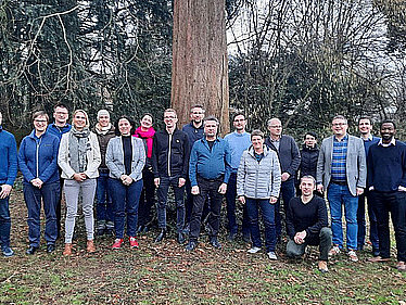 20 Personen haben sich unter einem großen Baum für ein Foto aufgestellt.