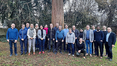20 Personen haben sich unter einem großen Baum für ein Foto aufgestellt.