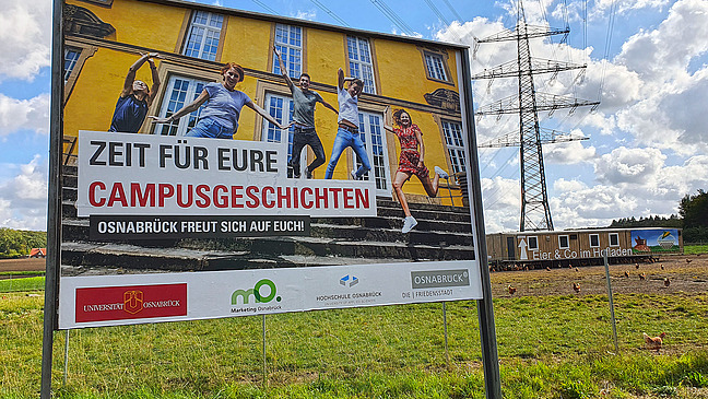 Ein gro&szlig;es Werbeplakat auf dem Studierende auf der Treppe des Schlosses in die Luft springen. Die Aufschrift lautet "Zeit f&uuml;r eure Campusgeschichten. Osnabr&uuml;ck freut sich auf euch!".