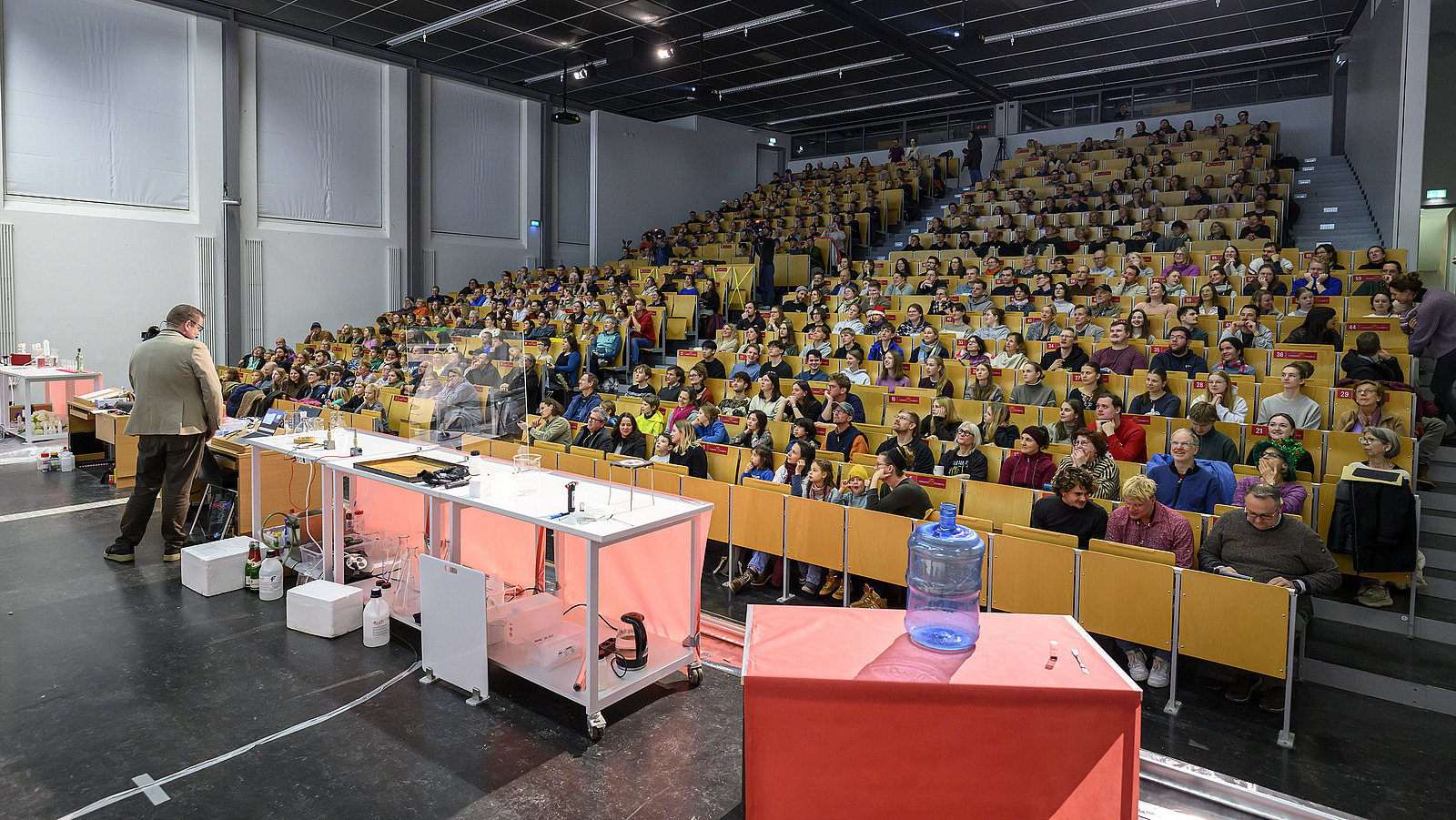 Personen in wei&szlig;en Kitteln unternehmen chemische Experimente in einem vollen Vorlesungssaal