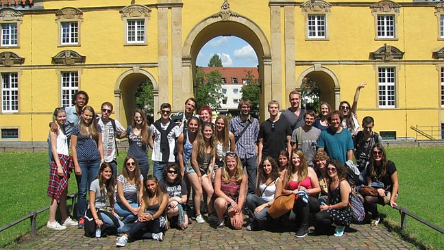 A group of international students and their chaperones from the International Office stand together in front of the entrance to Osnabrück University.