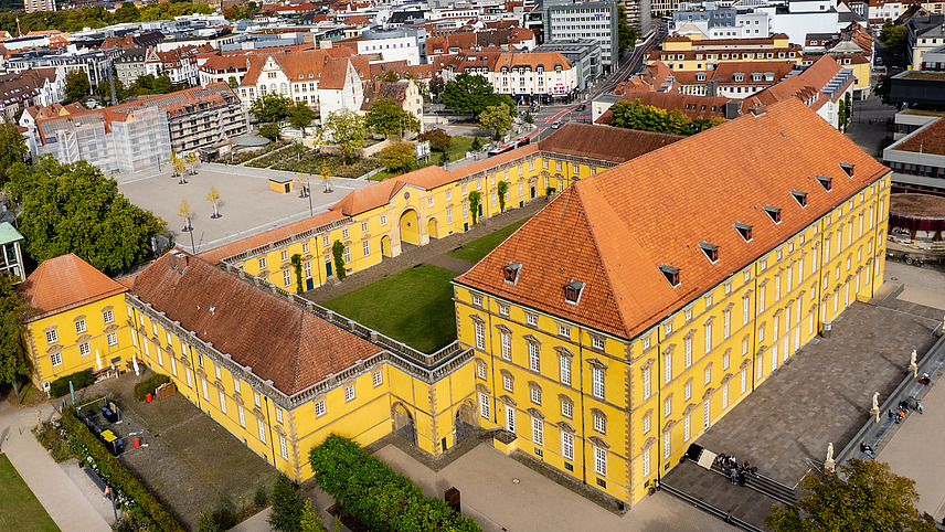 Drohnenaufnahme vom Schloss-Hauptgeb&uuml;ude mit Blick auf Innenhof und Stadt im Hintergrund