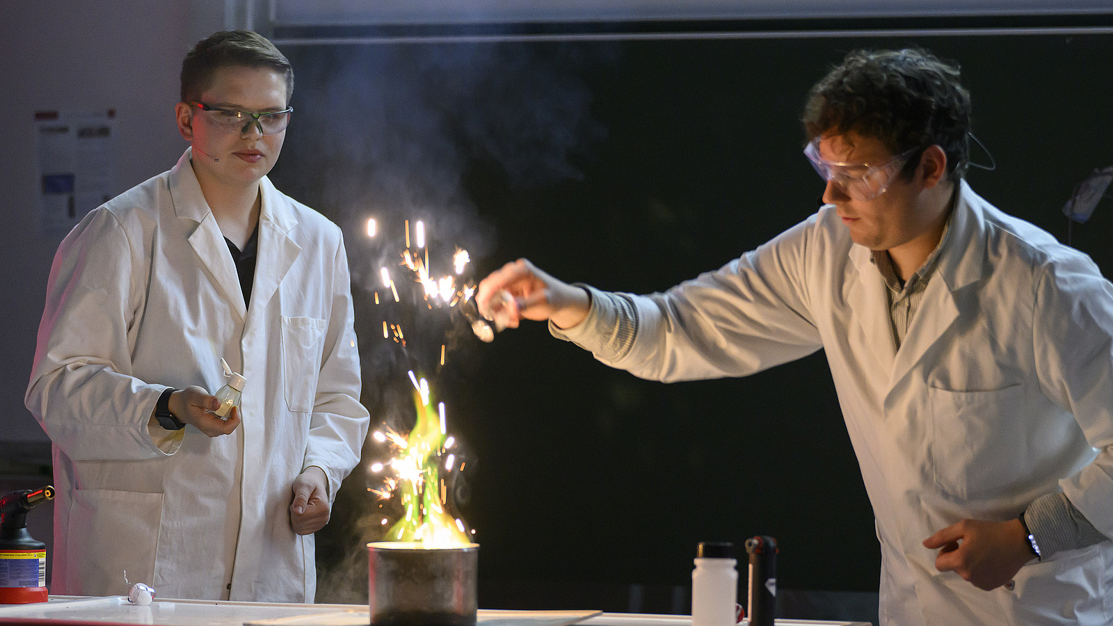Personen in wei&szlig;en Kitteln unternehmen chemische Experimente, dabei fliegen Funken