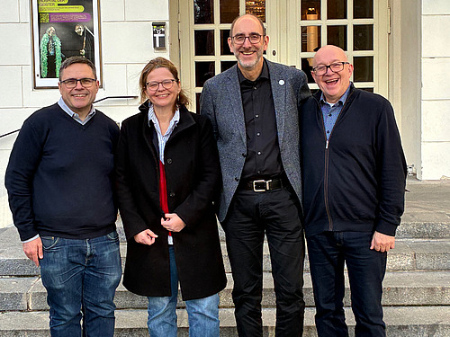 Three men and a woman stand next to each other and smile into the camera. 