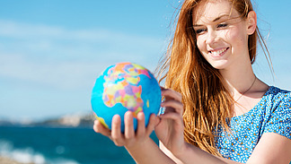 Junge Frau hält Globus am Meer in der Hand