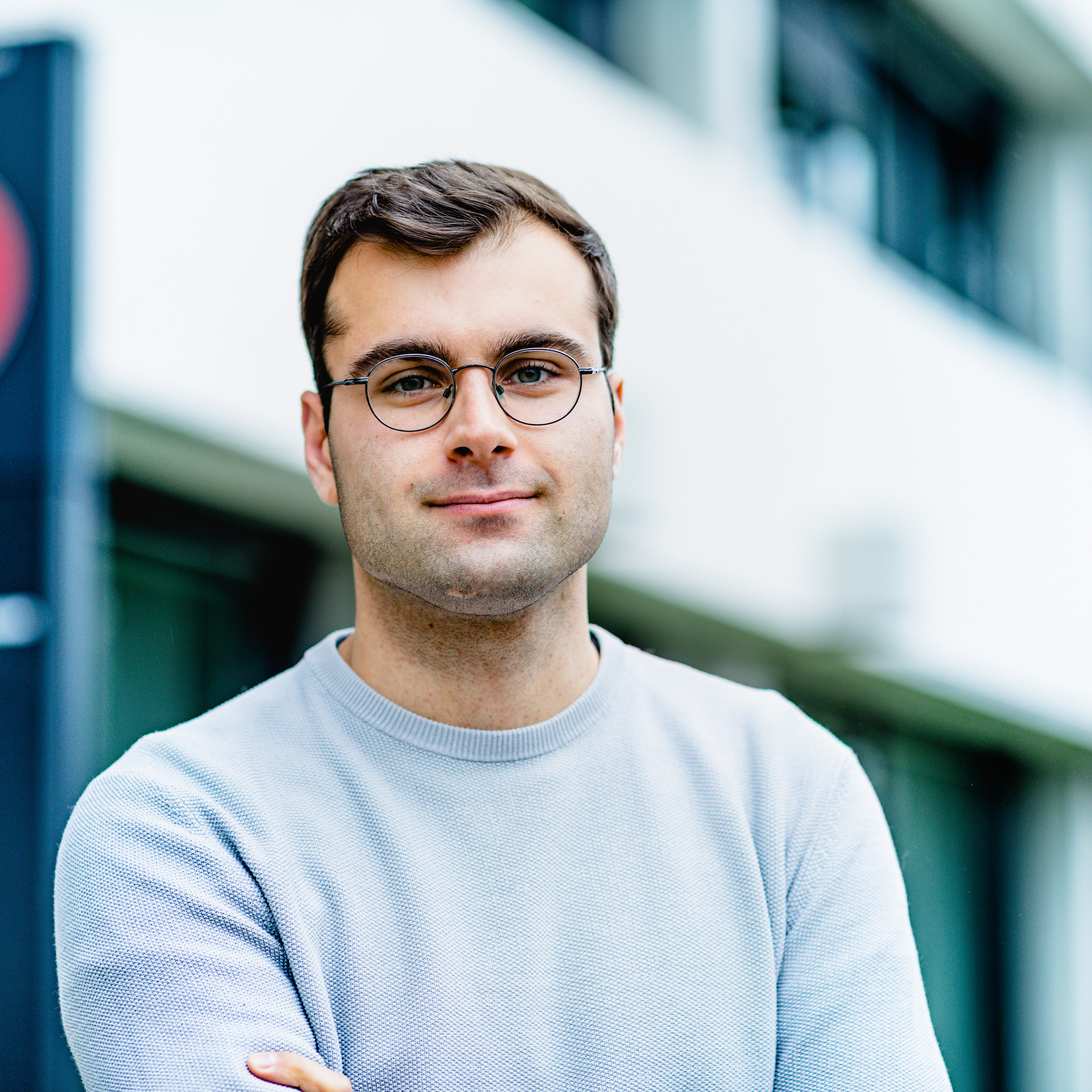 Das Bild zeigt Louis Loock vor dem Eingang des Instituts. Er lächelt mit verschränkten Armen in die Kamera.