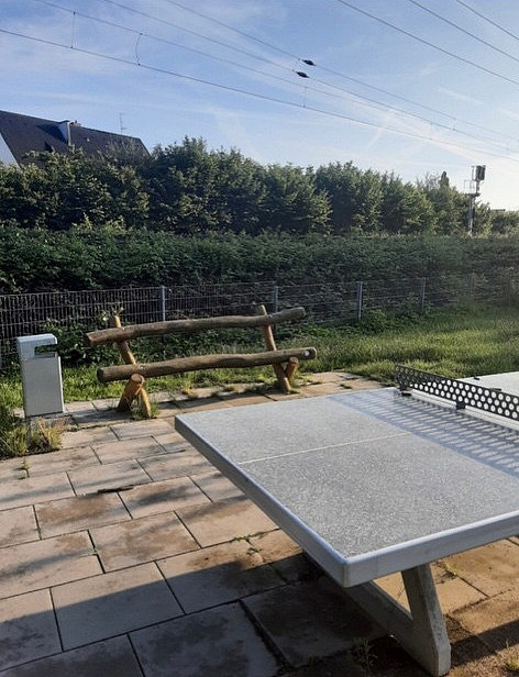 Ausschnitt einer Tischtennisplatte mit Sitzbank aus Holz im Hintergrund