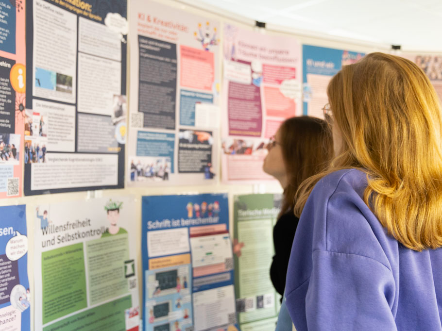 Zwei junge Frauen stehen vor einer Pinnwand, die mit bunten Plakaten bestückt ist