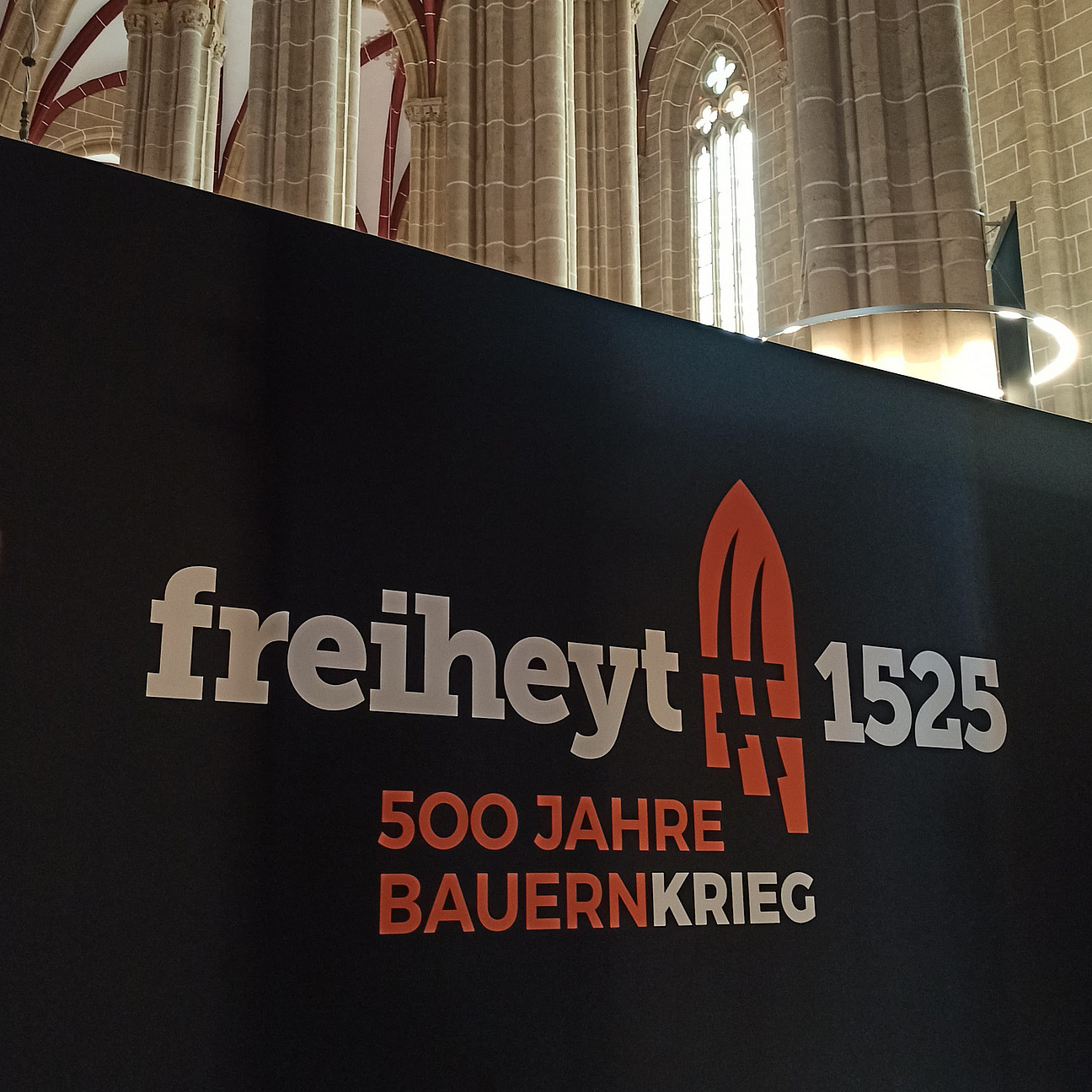 Das Bild zeigt den Innenraum einer Kirche. Im Vordergrund ist eine große schwarze Wand, auf der "freiheyt 2025" geschrieben steht.