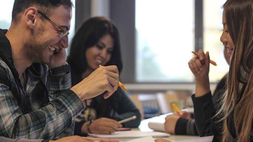 Three international students working together at a table and laughing.
