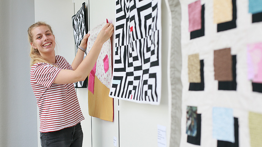 Eine Studentin hängt angefertigte Stoffmuster im Rahmen einer Ausstellung in ein Schaufenster.