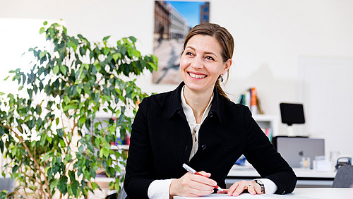 Ein Frau am Schreibtisch lächelt in die Kamera.