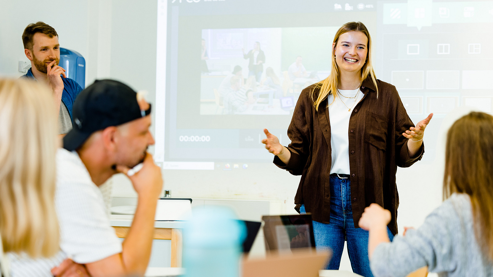 Eine Studierende pr&auml;sentiert im Rahmen eines Seminars. Im Hintergrund ist eine Videoaufzeichnung der Pr&auml;sentation zu sehen.