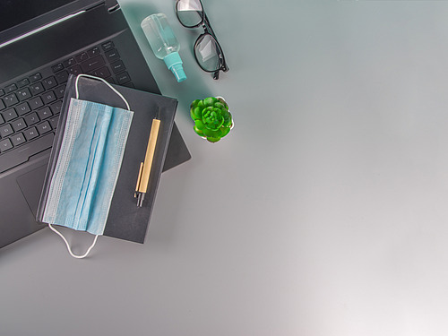 Laptop, medzinische Maske, Stift und Notibuch, Brille und ein Desinfetionsspray auf einer neutralen Ablagefl&auml;che