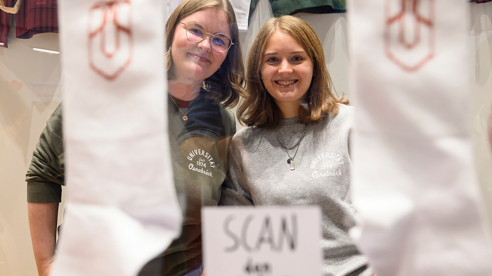 Two people look into the camera; in the foreground, you can see a pair of white socks with the university logo