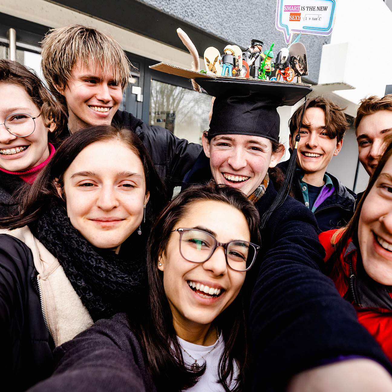 A selfie of several students, with a female student wearing a doctoral cap in the middle.