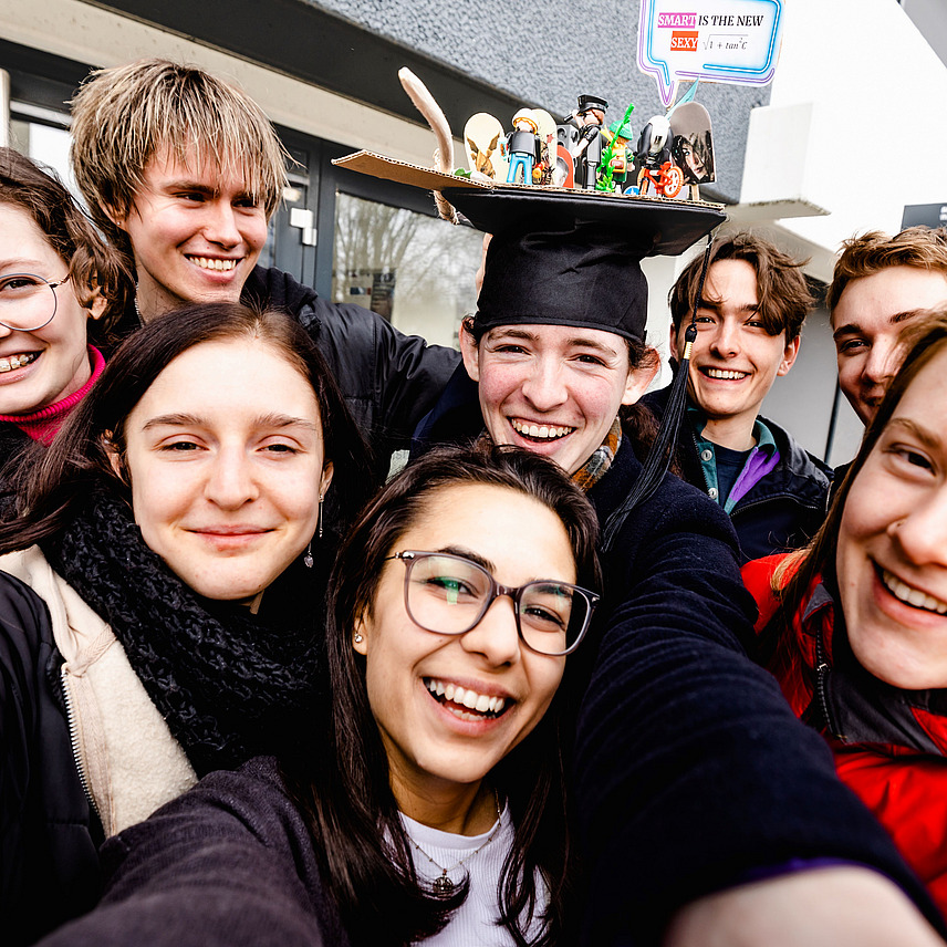 A selfie of several students, with a female student wearing a doctoral cap in the middle.