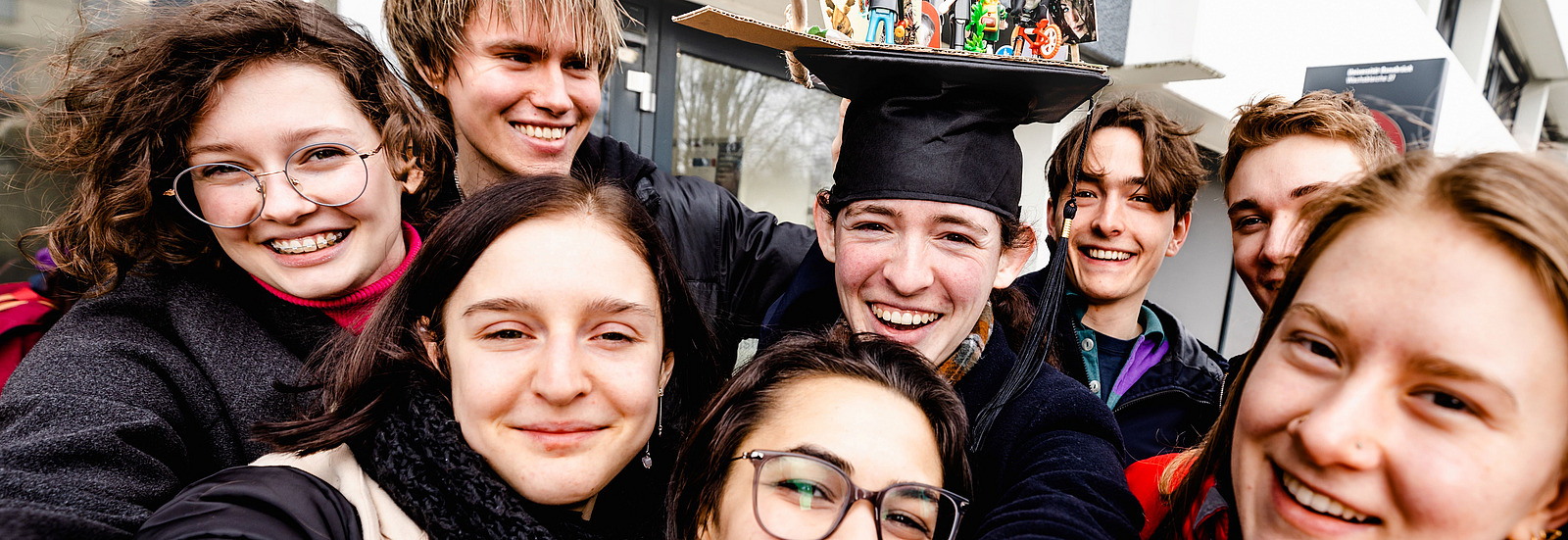 A selfie of several students, with a female student wearing a doctoral cap in the middle.