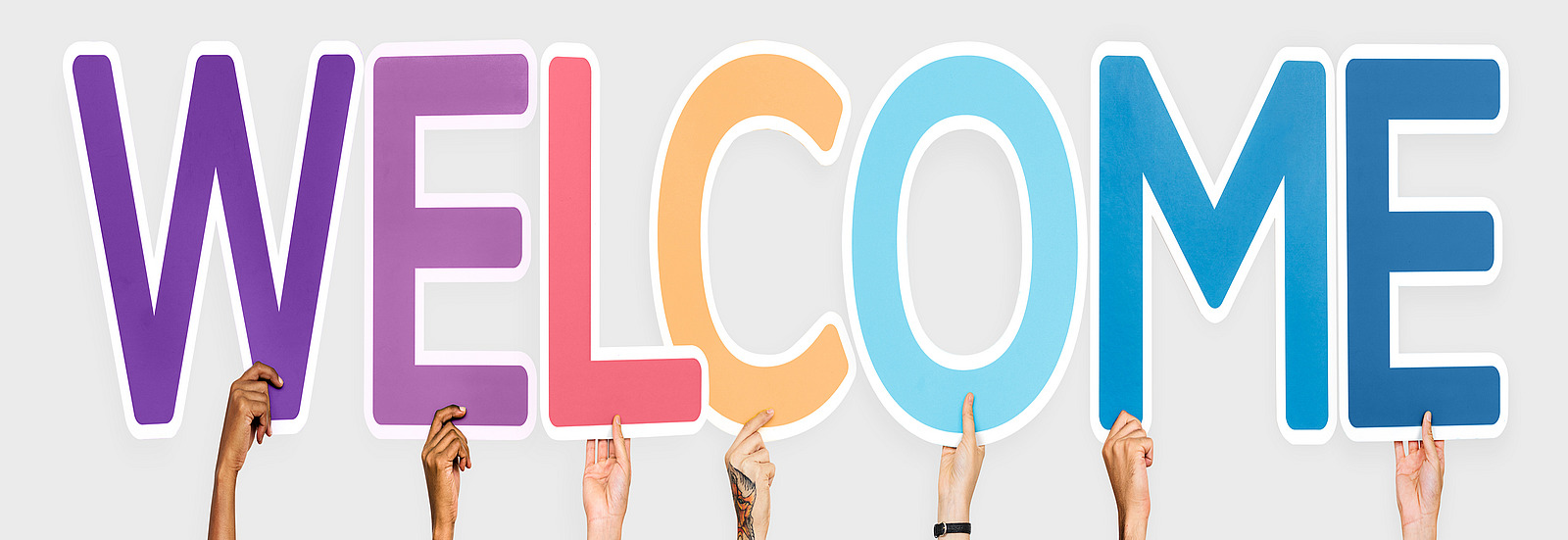 Different hands hold up various colored letters that together form the word “WELCOME”.