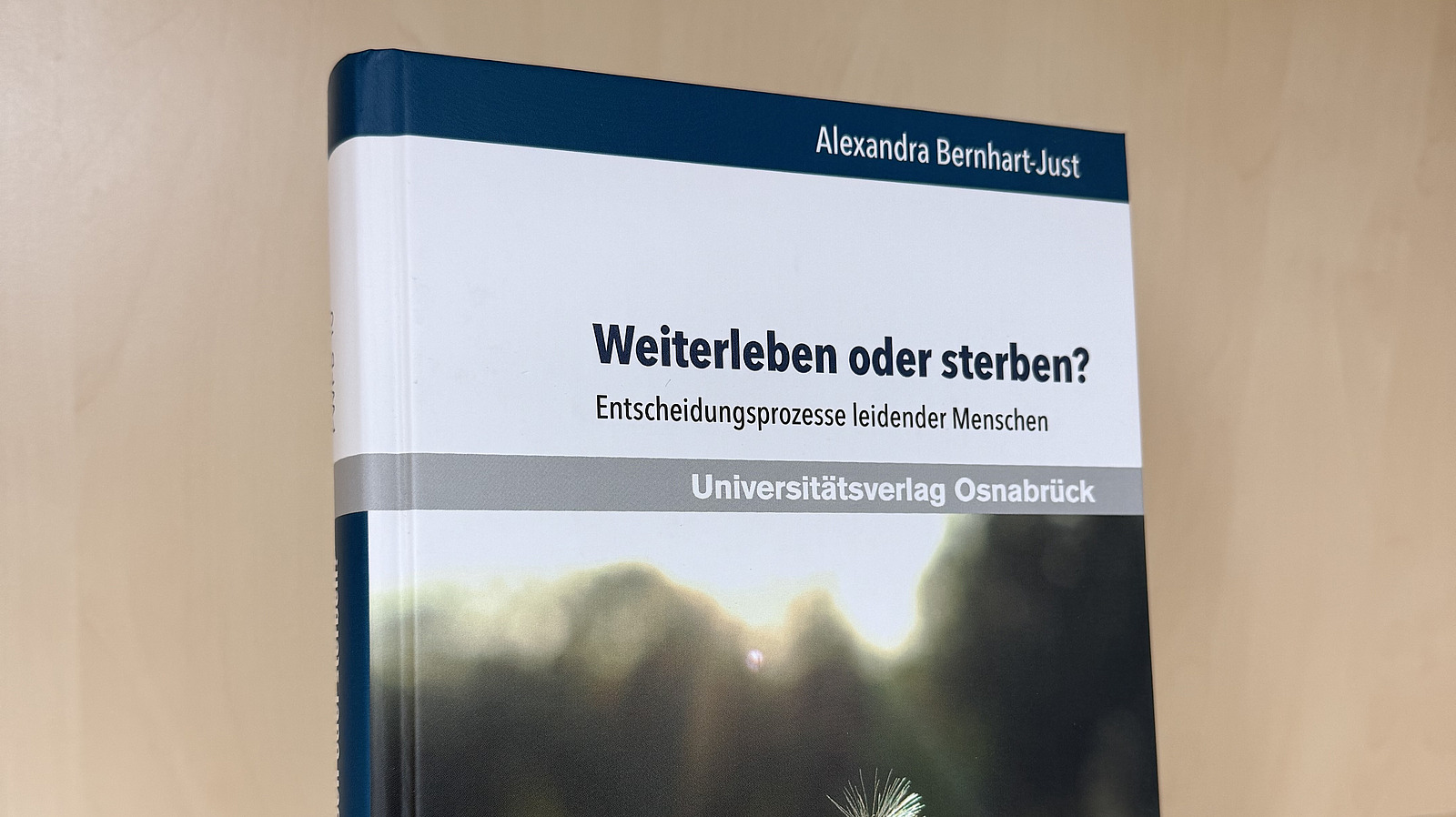 Ein Fachbuch von Alexandra Bernhart-Just mit dem Titel "Weiterleben oder sterben? Entscheidungsprozesse leidender Menschen" steht in einem Regal.