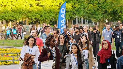 Many young people are walking through the castle park to a DAAD event for which banners have been put up. Everyone is wearing business cards on a pendant around their neck.