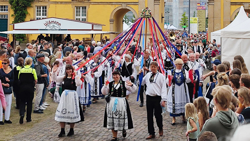 Festive procession with maypole and people wearing traditional costumes.