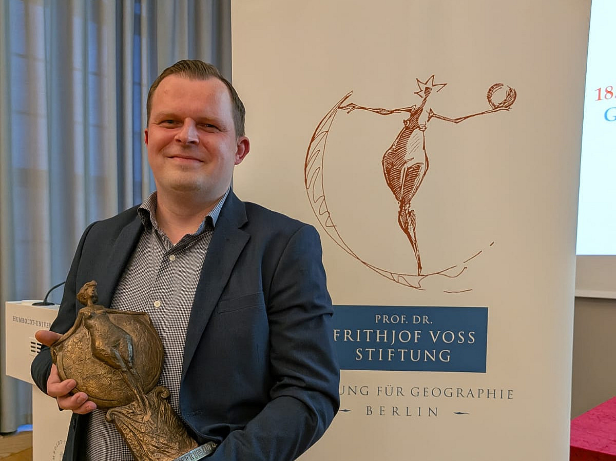 Ein Mann steht vor einem Plakat und hält eine kleine Statue in der Hand. 