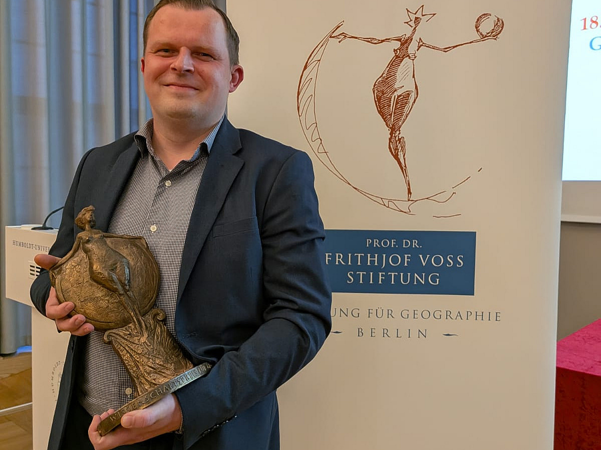 A man stands in front of a poster and holds a small statue in his hand. 