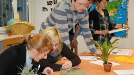 Sch&uuml;lerinnen und Sch&uuml;ler sitzen an einem Tisch und betrachten Pflanzen