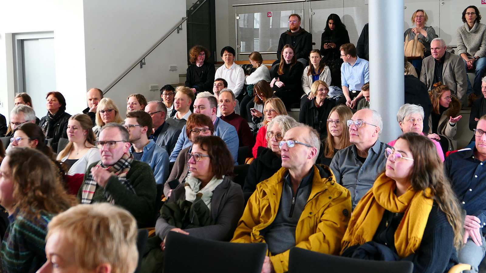 Viele Personen sitzen in Stuhlreihen.