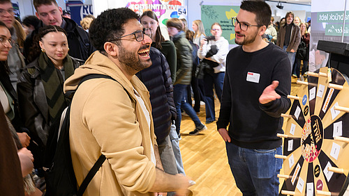 A person stands laughing at a wheel of fortune