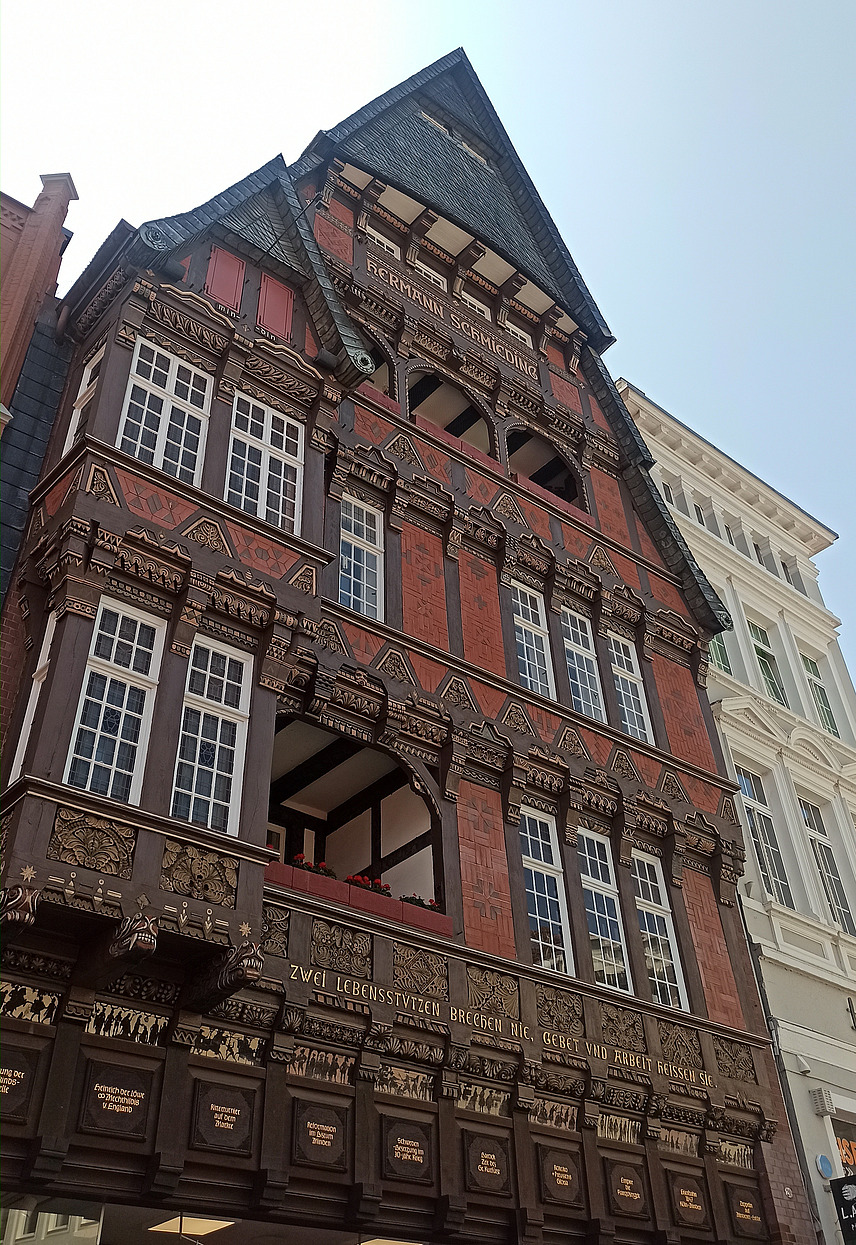 Das Bild zeigt ein reich verziertes Fachwerkhaus mit detaillierten Schnitzereien und Inschriften an der Fassade.