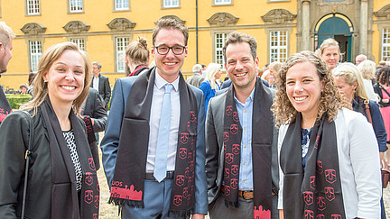 Vier festlich gekleidete, promovierte Personen tragen den Promotionsschal