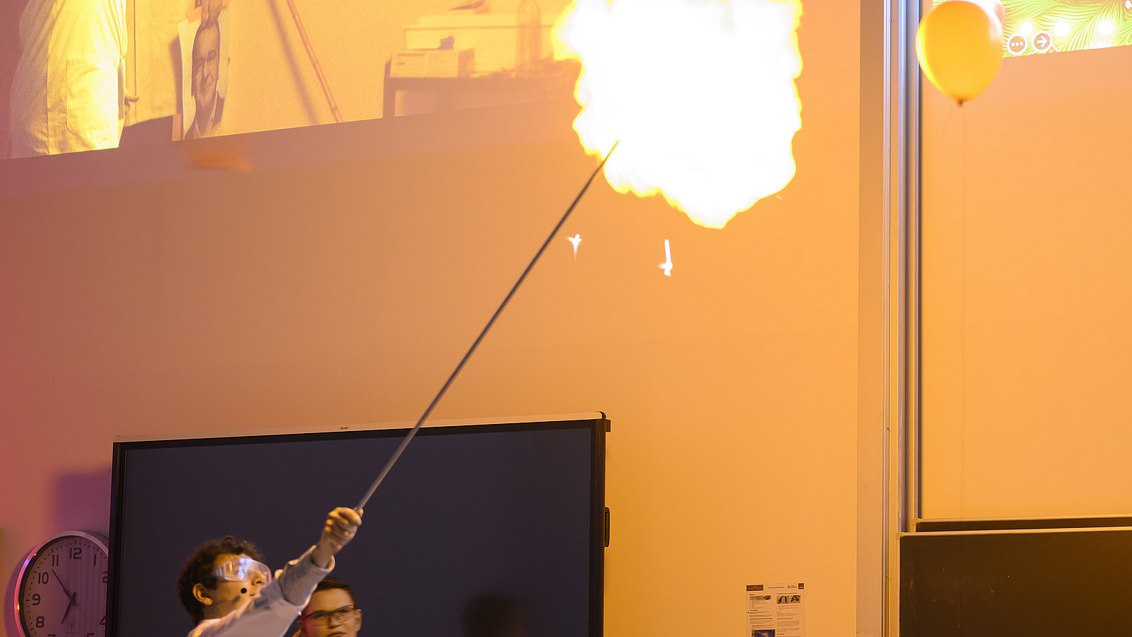 Personen in wei&szlig;en Kitteln unternehmen chemische Experimente, dabei entsteht eine Flamme