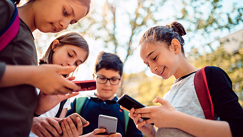 Schülerinnen und Schüler stehen auf dem Pausenhof und blicken auf ihre Smartphones. 
