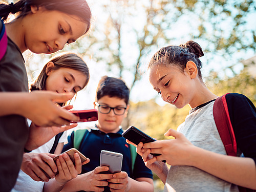 Schülerinnen und Schüler stehen auf dem Pausenhof und blicken auf ihre Smartphones. 