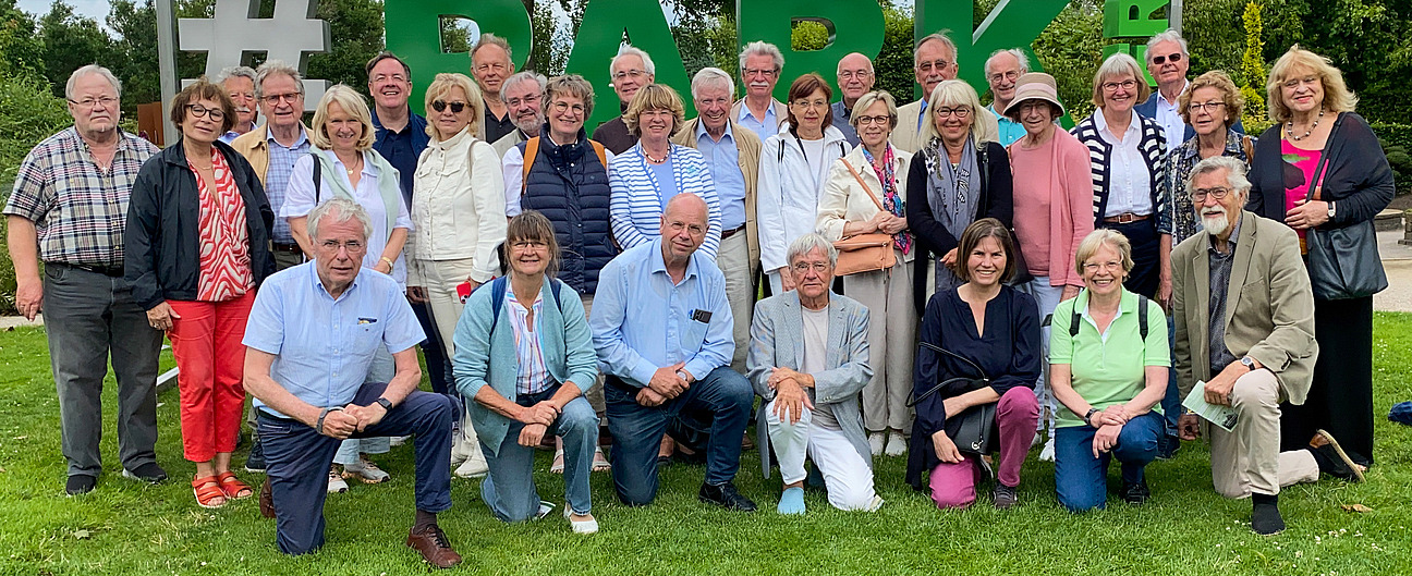 Gruppe von Erwachsenen in Freizeitkleidung posiert vor gro&szlig;en gr&uuml;nen Buchstaben auf einer Wiese im Freien