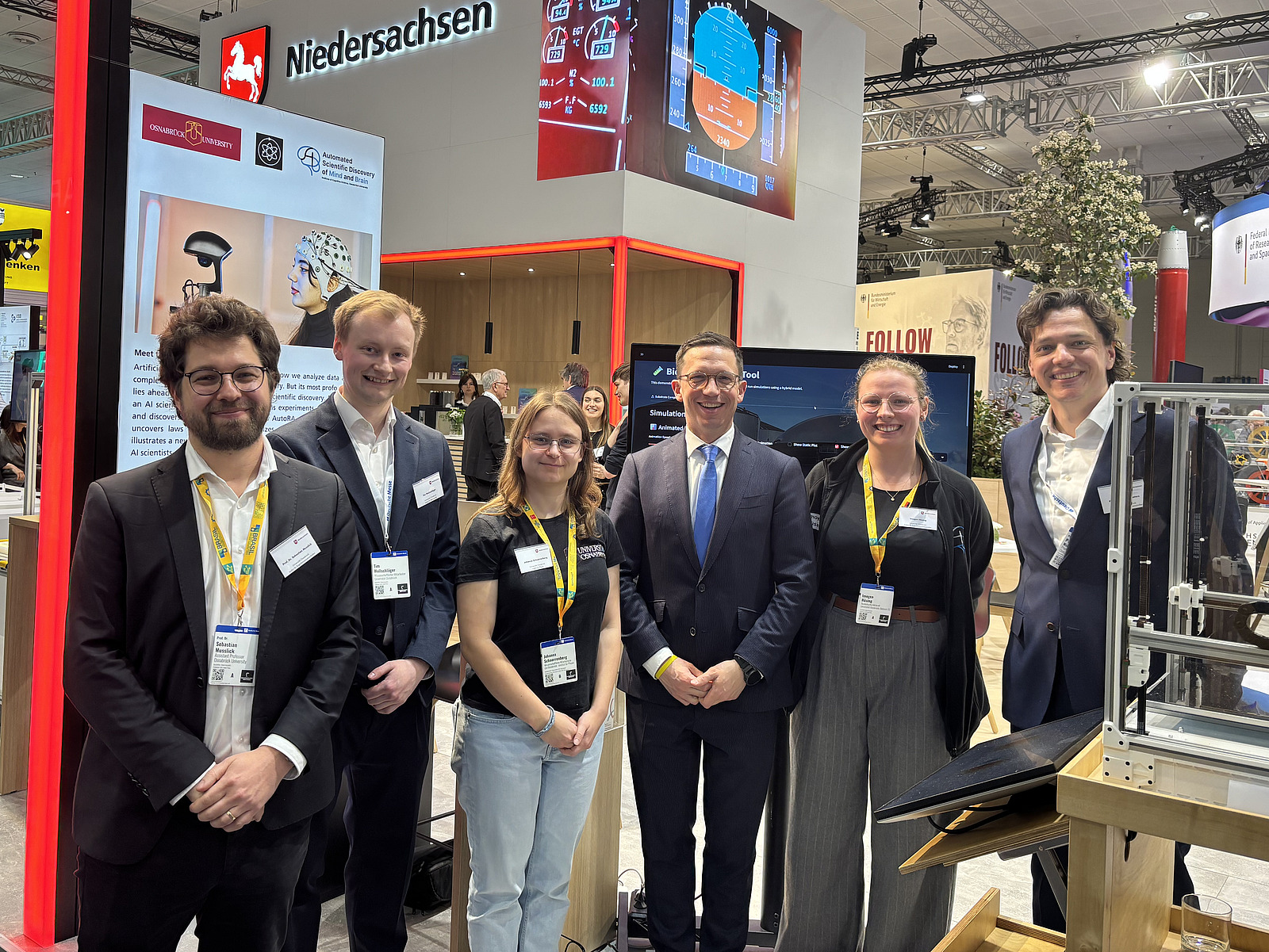 Zwei Frauen und drei M&auml;nner stehen vor einem Messestand. 