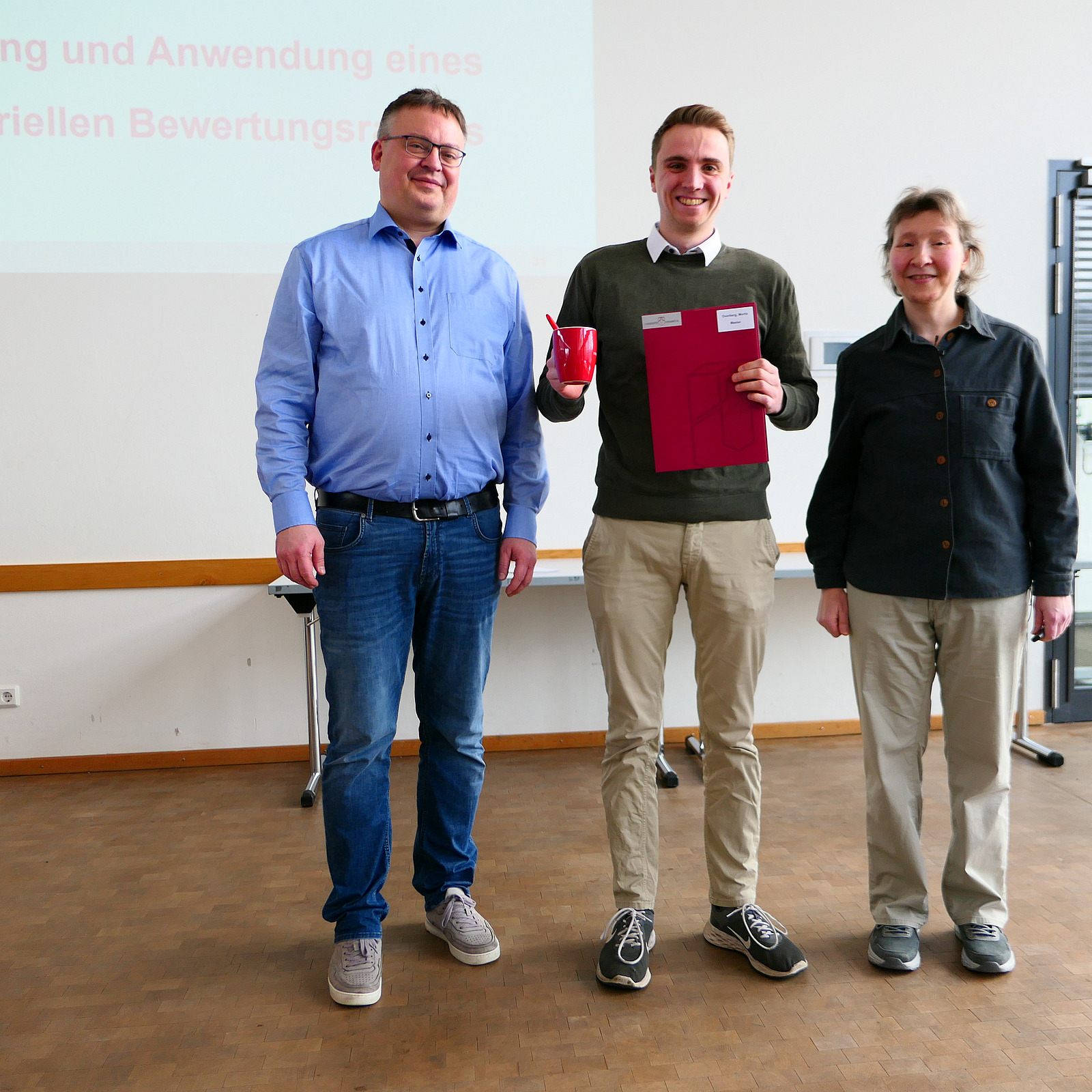 Ein Student steht mit seinem Abschlusszeugnis zwischen Dekan und Studiendekanin.
