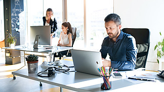 Three business people at work. Two women and a man sit in the office and work together.