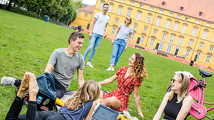 Vier Studierende sitzen auf einer Decke im Schlossgarten und unterhalten sich.