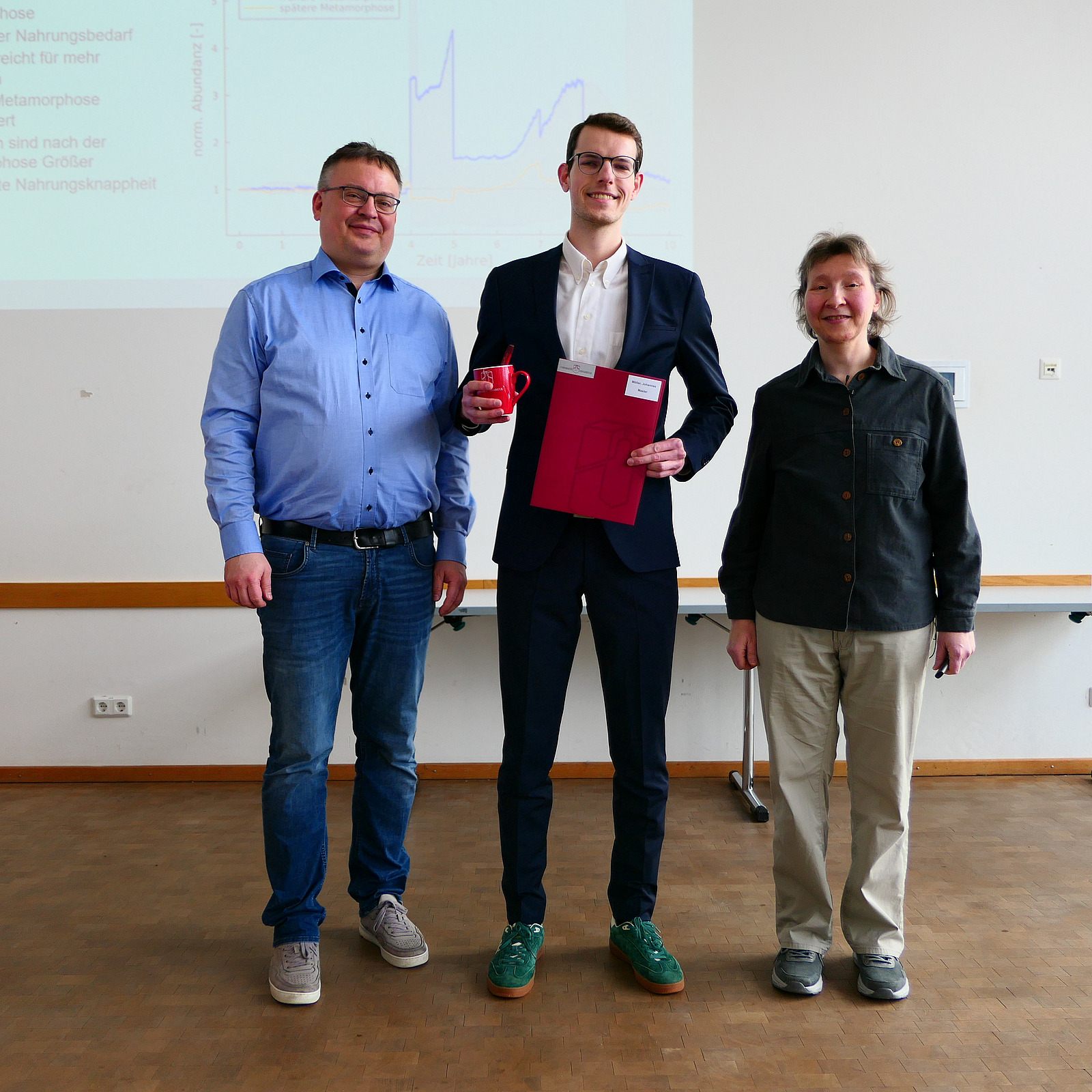 Ein Student steht mit seinem Abschlusszeugnis zwischen Dekan und Studiendekanin.