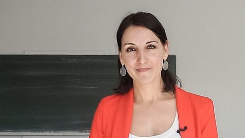 Kerstin Bartscherer steht vor einer Schiefertafel und l&auml;chelt in die Kamera