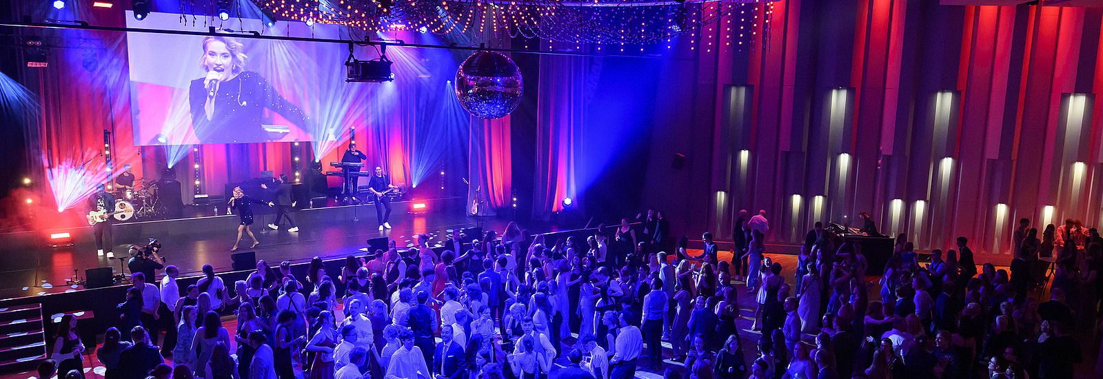 Mehrere festlich gekleidete Personen auf der Tanzfläche eines Ballsaals